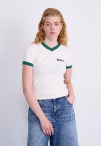 Balta trumpomis rankovėmis marškinėliai su žalia V formos iškirpte ir žaliais rankogaliais, ant kairiojo krūtinės puikuojasi mažas žalias "Dickies" logotipas. Dėvimi su mėlynomis džinsinėmis kelnėmis.