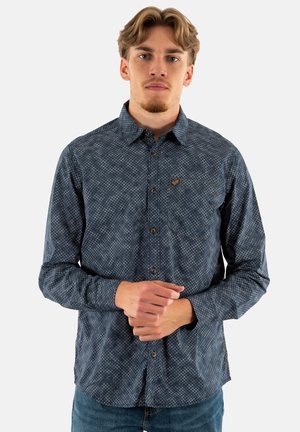 Chemise à manches longues en tissu bleu foncé, avec un motif géométrique, un boutonnage sur le devant et un petit logo sur la poche poitrine.