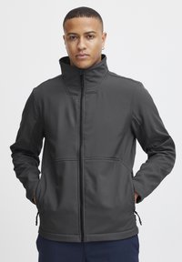 Grå softshell-jakke med høj krave, frontlynlås og to sidelommer. Har en glat tekstur og artikulerede syninger.