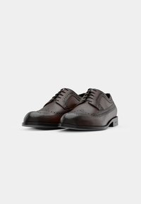 Zapatos de vestir de cuero marrón con intrincados detalles de brogue, puntera redondeada y un acabado suave. Suela plana con un sutil logo en el lateral.