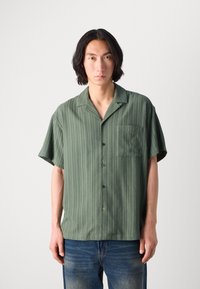 Short-sleeve, green striped shirt with a pocket, button placket, and soft texture, paired with blue jeans.
