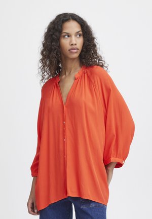 Luftig orange bluse med V-hals, knaplukning foran og trekvartærmer. Fremstillet af letvægtsstof med en tekstureret overflade.