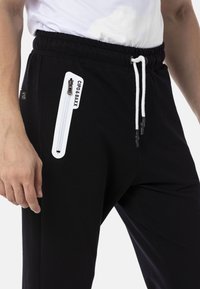 Schwarze Jogginghosen aus Baumwollmischung mit einem elastischen Bund und Kordelzug, einer seitlichen Reißverschlusstasche und einem Logodetail auf der Tasche.