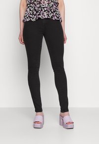 Jeans skinny pretos combinados com sandálias de plataforma lilás claro. Os saltos têm um acabamento texturizado, complementando o design ajustado dos jeans.