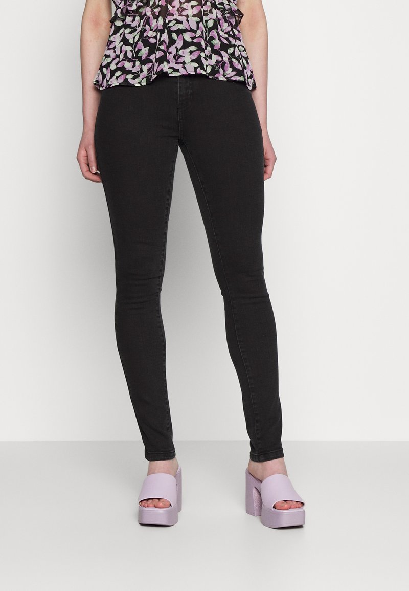 Jeans skinny pretos combinados com sandálias de plataforma lilás claro. Os saltos têm um acabamento texturizado, complementando o design ajustado dos jeans.