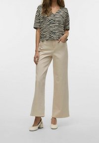 Haut à manches courtes rayé noir et beige, associé à un pantalon large beige et des chaussures à talons blocs de couleur claire. Fond uni.