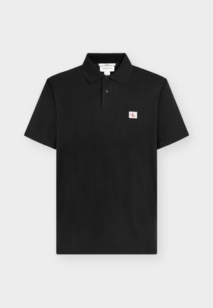 Schwarzes kurzärmeliges Poloshirt mit zwei Knöpfen und einem kleinen weißen und roten "CK"-Logo-Patch auf der linken Brust.