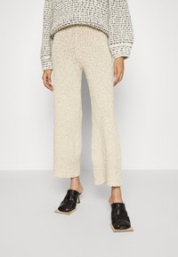 Cremfarbene, gestrickte weit geschnittene Hose mit strukturiertem Finish, kombiniert mit offenen schwarzen Absatzmules. Der Pullover hat ein kariertes Muster in Grautönen.