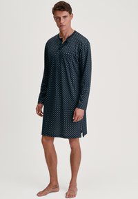 Marineblaue Nachthemd mit langen Ärmeln und kleinen weißen Punkten, ausgestattet mit einem geknöpften Henley-Ausschnitt und seitlichen Schlitzen für mehr Bewegungsfreiheit.