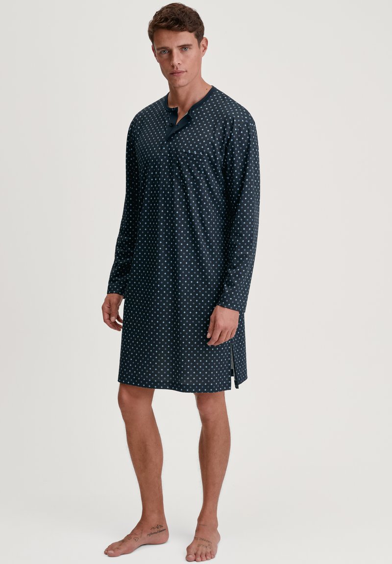 Camicia da notte blu navy a maniche lunghe con piccoli pois bianchi, dotata di collo henley con bottoni e fessure laterali per una maggiore facilità di movimento.