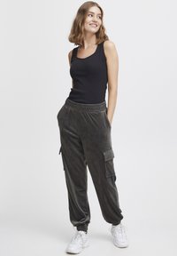 Zwart geribbeld tanktop gecombineerd met donkergrijze velours cargobroek, met zijzakken en geplooide enkels, gedragen met witte sneakers.