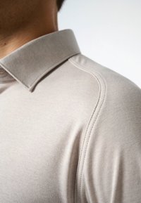 Beige poloshirt met een kraaghalslijn, voorzien van een textuurstof en accentstiksel langs de schouder voor een op maat gemaakte uitstraling.