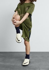 Vihreä urheilupaita, jossa on lyhyet hihat ja Dri-FIT-tekniikka. Paidassa on Paris Saint-Germainin logo, ja se on yhdistetty laivastonsinisiin sukkiin ja kermaisiin Nike-jalkineisiin.