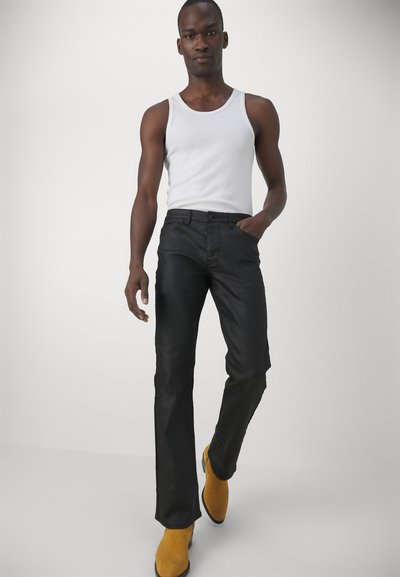 Schwarze Jeans im Slim-Fit, aus Denim mit leichtem Glanz. Kombiniert mit einem weißen Tanktop und gelben Stiefeletten. Schlichte Nähte.