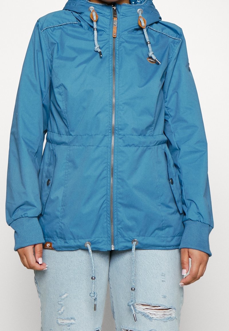 Veste légère bleue avec fermeture éclair, capuche ajustable et cordons à la taille et à l'ourlet. Comprend des poignets côtelés et des poches latérales.