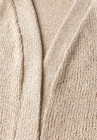 Beige cardigan med en texturerad stickad mönster, med en djup V-hals och öppen framdesign. Mjuk material med subtila ljusa trådar.