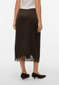 Falda midi de satén color marrón con dobladillo de encaje recortado, textura suave y talle ajustado. Combinada con tacones oscuros y una blusa clara.