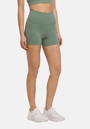 Groene high-waisted shorts gemaakt van rekbaar materiaal, met een gladde textuur en een eenvoudig ontwerp. Gecombineerd met witte sportschoenen.