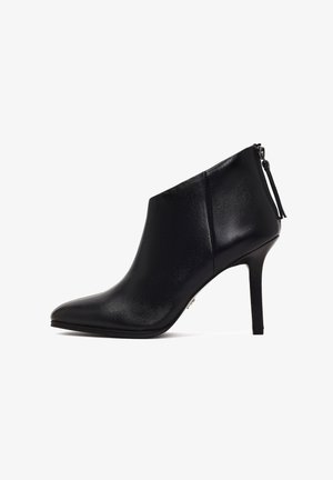 Bota de tobillo de cuero negro con punta afilada, alto tacón de aguja y cierre con cremallera lateral. Textura suave sin patrones ni acentos.