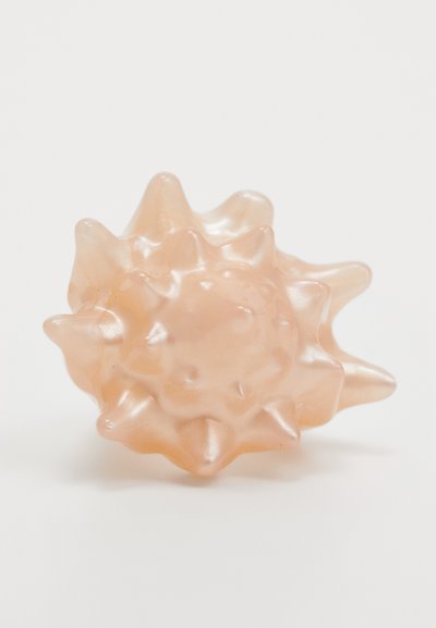 Sculptură translucidă de culoare piersică, asemănătoare unei ființe marine, cu o suprafață ascuțită și o formă rotundă. Textură netedă cu margini evidențiate.