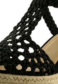 Černá tkaná sandal s propracovaným pleteným vzorem, plochou espadrilovou podešví s přírodní juteovou detailem a béžovou vnitřní stélkou.
