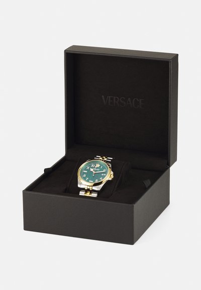 Montre Versace dans une boîte noire, avec un cadran vert, un bracelet doré et argenté, des chiffres arabes et un boîtier en acier inoxydable poli.