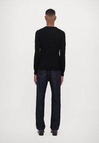 Maglione nero lavorato a maglia e jeans in denim blu scuro. Il maglione ha una scollatura rotonda e maniche lunghe, mentre i jeans hanno una vestibilità comoda.