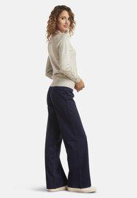 Light gray sweater with long sleeves and a ribbed hem, paired with navy wide-leg pants and beige sneakers. Smooth texture and relaxed fit.