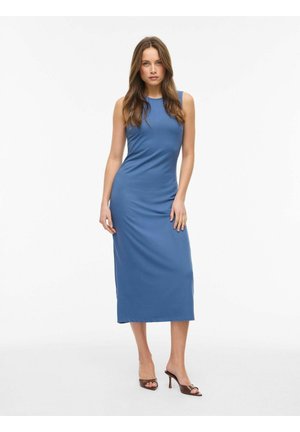 Kobieta stojąca twarzą do przodu, ubrana w niebieską sukienkę midi bez rękawów i brązowe sandały na obcasie na jednolitym białym tle.