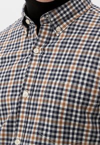 Overhemd met knoopsluiting in een marineblauw, bruin en wit geruit patroon. Katoenen stof met een klassieke kraag en een borstzakdetail.