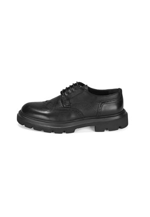 Chaussure en cuir noir à lacets avec empeigne texturée, bout arrondi et semelle en caoutchouc épaisse comportant des motifs d'adhérence.