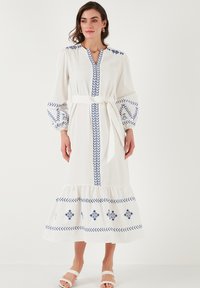 White long dress with blue embroidered patterns, balloon sleeves, a V-neckline, and a tied waist. Features a tiered hemline and soft texture.