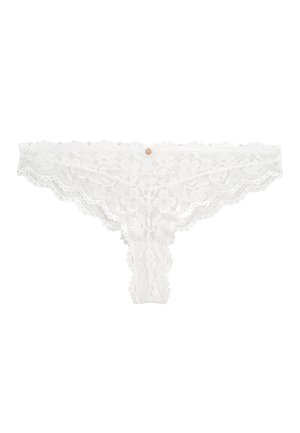 String blanc en dentelle florale avec des bords festonnés et un petit charme métallique circulaire au centre de la ceinture.