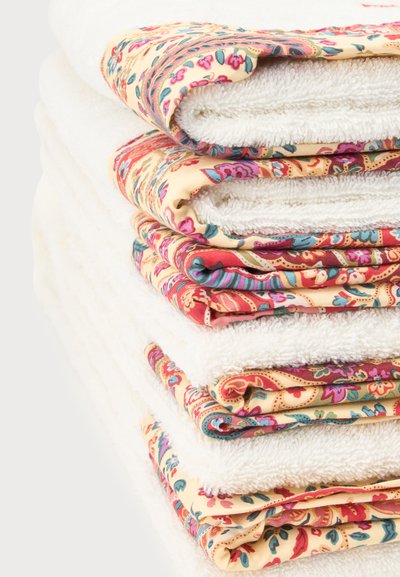 Pile de serviettes blanches avec des bords à motifs floraux colorés, pliées soigneusement sur un fond blanc.
