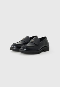 Black leather loafers with a smooth texture, round toe, and a cushioned sole. Features a stitched design and a gold logo accent on the strap.
