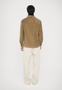 Smeđi kadifasti sako s ovratnikom i leđnom ušicama, s dugim rukavima, zakopčanim manžetama i blago zaobljenim rubom. Uparen s krem hlačama.