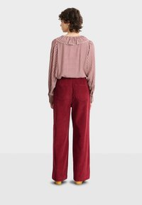 Pantaloni a gamba larga in corduroy rosso con una finitura testurizzata e due tasche posteriori, abbinati a una blusa a fantasia con scollatura e polsini a volant.