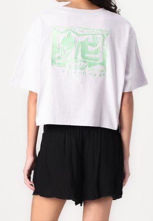 Biały krótki t-shirt z zielonym nadrukiem na plecach, w zestawie z czarnymi plisowanymi szortami; miękki bawełniany materiał, luźny krój.