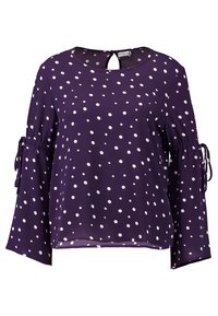 Blouse violette à pois blancs, col rond et manches longues avec liens aux poignets. Tissu léger et fluide. Détail dos ouvert.