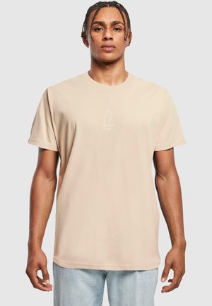 Beige katoenen t-shirt met een ronde hals, korte mouwen en een wit surflogo in het midden van de borst. Ontspannen pasvorm, zachte textuur.