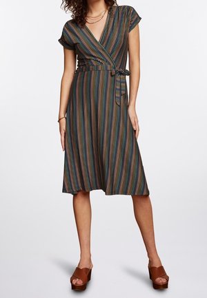 Femme portant une robe portefeuille courte à manches courtes, longueur genou, avec des rayures multicolores verticales et des sandales compensées marron.