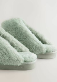 Fuzzy mint green slippers with a plush texture and thick soles, featuring a subtle logo on the side. Open-toe design and cozy aesthetic.