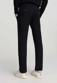 Czarnie spodnie bawełniane o prostym kroju, z dwiema tylnymi kieszeniami i teksturowanym paskiem. Połączone z białymi sportowymi butami.