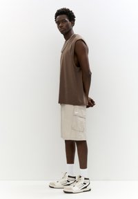 Maglietta smanicata marrone, pantaloni cargo beige chiaro con tasche, calzini bianchi e scarpe da ginnastica alla moda multicolori. Design semplice e sportivo.