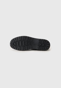 Talpa de pantof din cauciuc negru cu modele adânci de profil, inclusiv designuri zigzag și chevron. Textură netedă și material durabil vizibile.