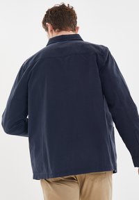 Giacca in cotone blu navy con colletto e maniche lunghe, caratterizzata da una linea dritta e tasche laterali, vista da dietro.