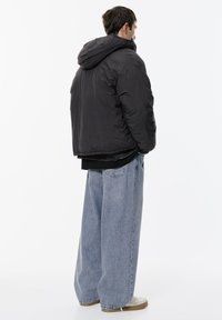 Jachetă puffer neagră cu glugă, croi relaxat, asortată cu blugi oversized de un albastru deschis. Jacheta are o textură netedă și un design minimalist.