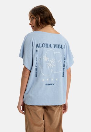 T-shirt bleu clair à manches courtes avec une coupe ample. Présente un graphique floral blanc et le texte "ALOHA VIBES" et "ÉTAT D'ESPRIT D'ÉTÉ."