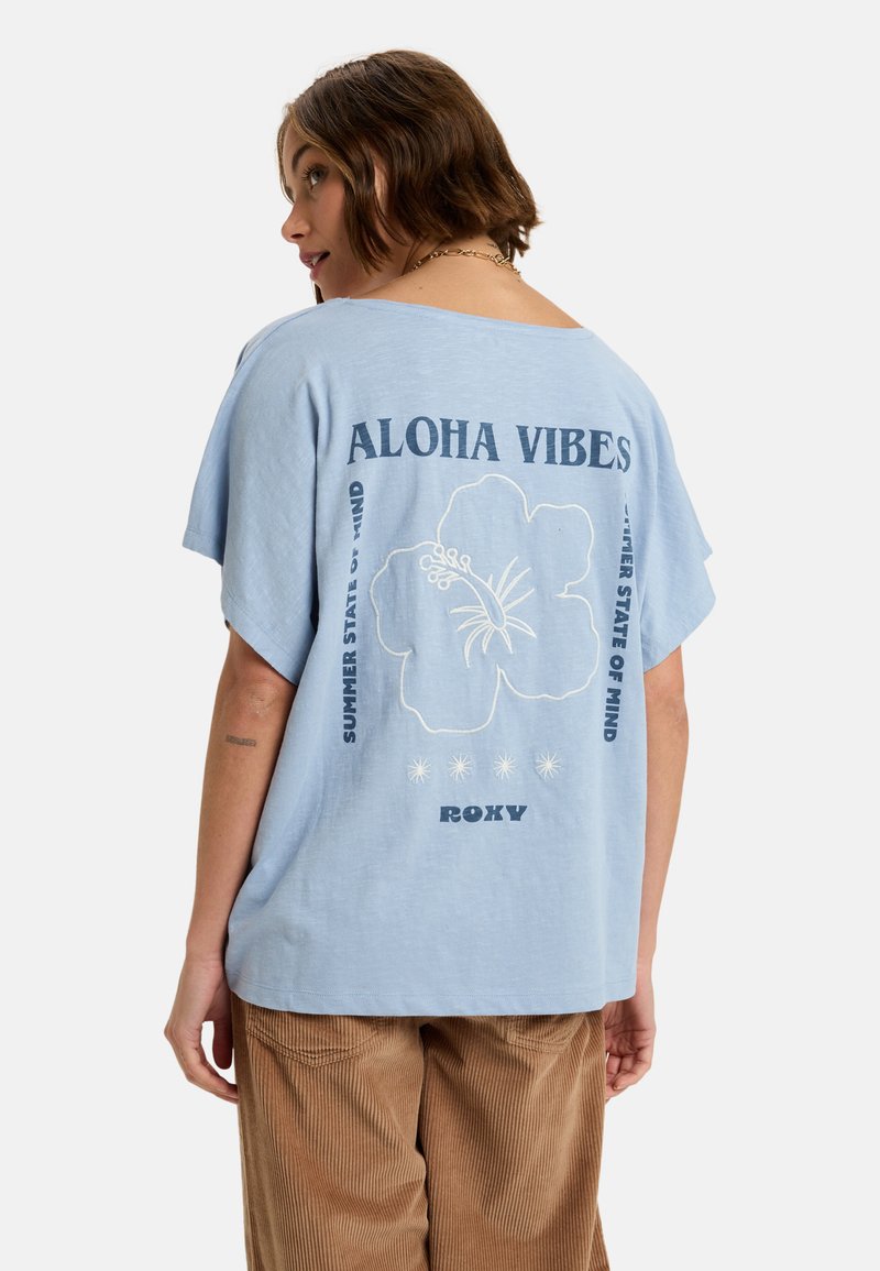 Lys blå, kortærmet t-shirt med løs pasform. Har hvidt blomsterdesign og teksten "ALOHA VIBES" samt "SUMMER STATE OF MIND."