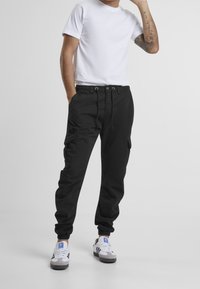 Zwarte cargobroek met een elastische tailleband en trekkoord, voorzien van zijzakken en taps toelopende boorden. G gedragen met een wit T-shirt en sneakers.
